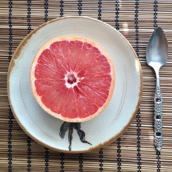 Pink grapefruit slice in half sits on a plate.